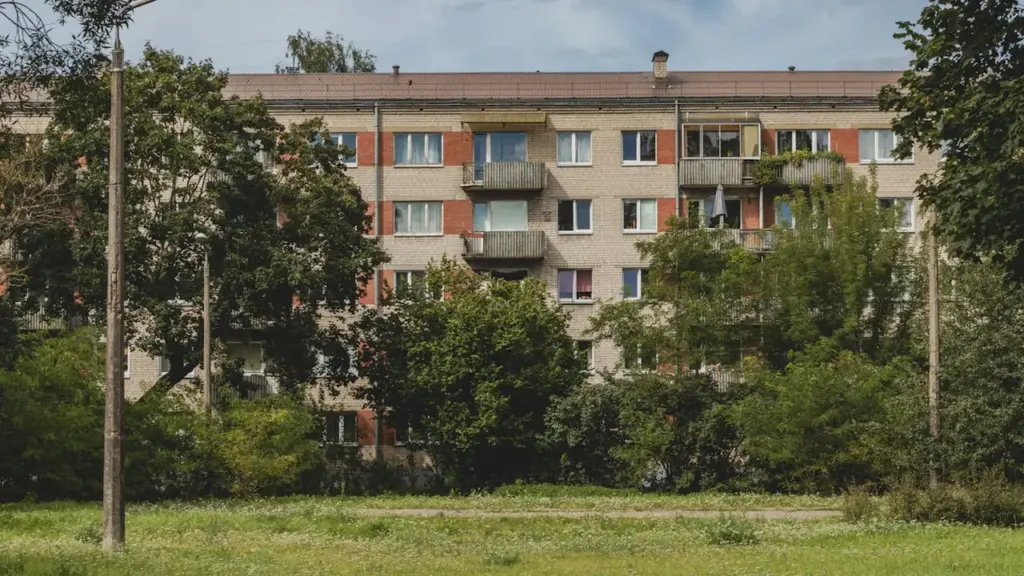 Hruščova laika daudzdzīvokļu nams Rīgas mikrorajonā, kuru ieskauj koki un zaļā zona.