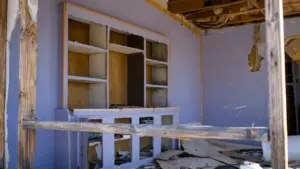Iekštelpas skats uz izpostītu māju ar sagrautu plauktu un būvgružiem uz grīdas.